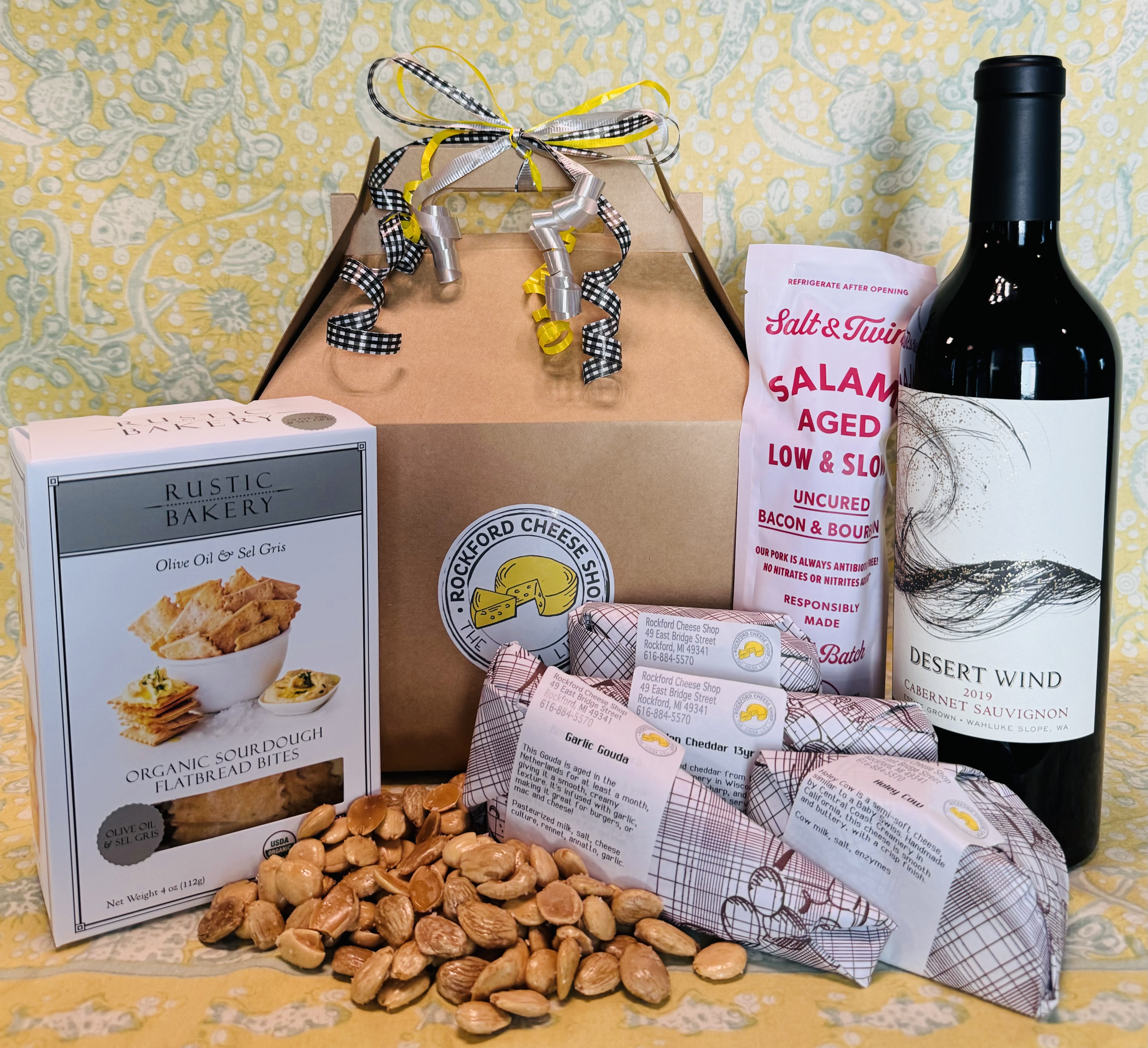 A Rockford Cheese Shop gift box with crackers, salami, a bottle of cabernet, almonds, and wrapped cheeses.