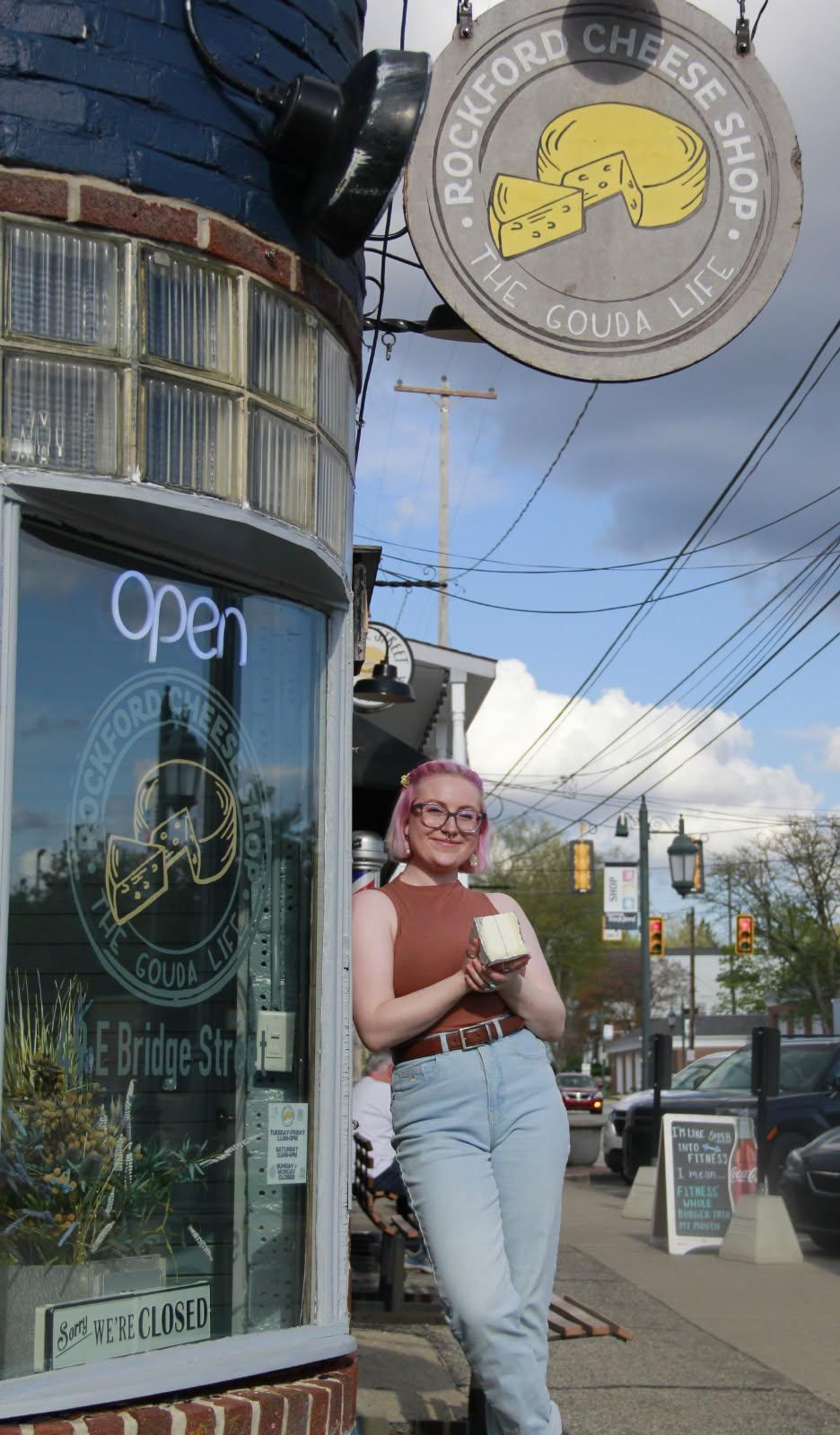 The Rockford Cheese Shop storefront on Bridge Street with a staffer standing under the round hanging sign.